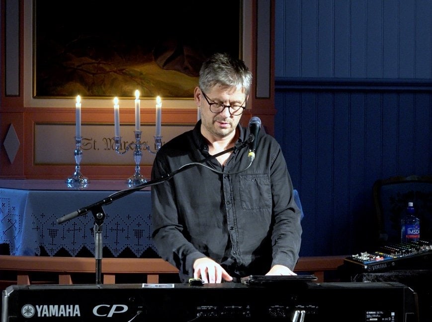 Musiker spiller piano under kirkekonsert i Fosen, med levende lys og tradisjonell kirkeatmosfære.